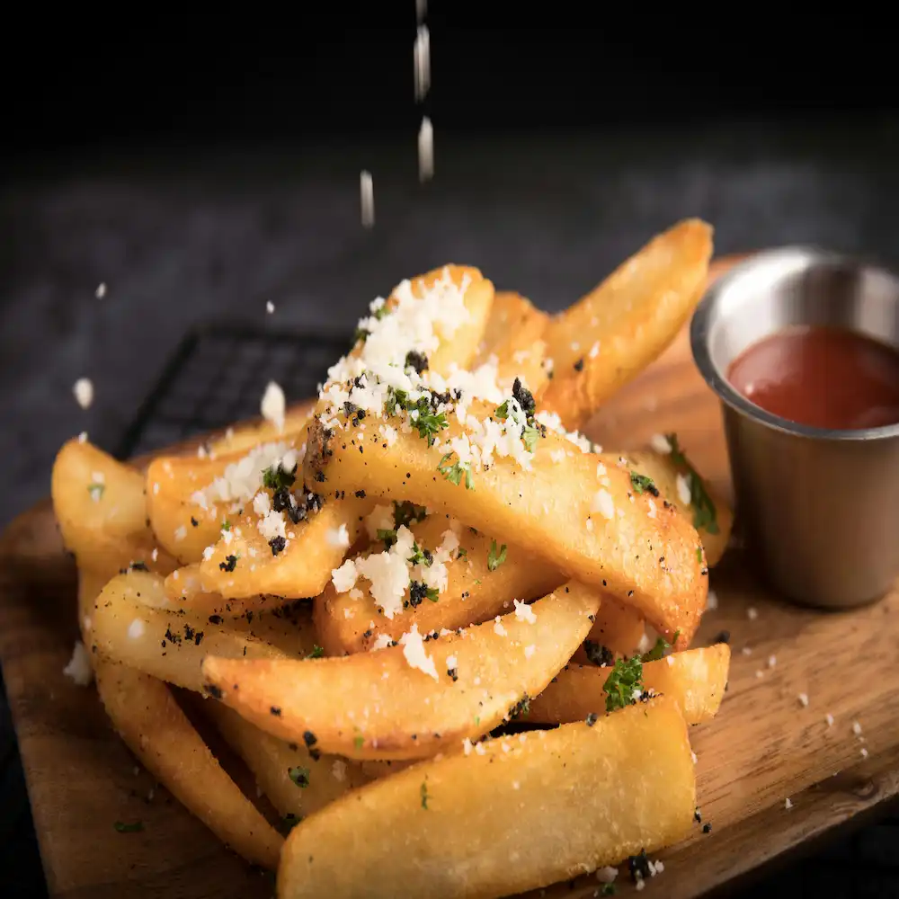 A close up image of fries getting seasoned with salt and herbs.